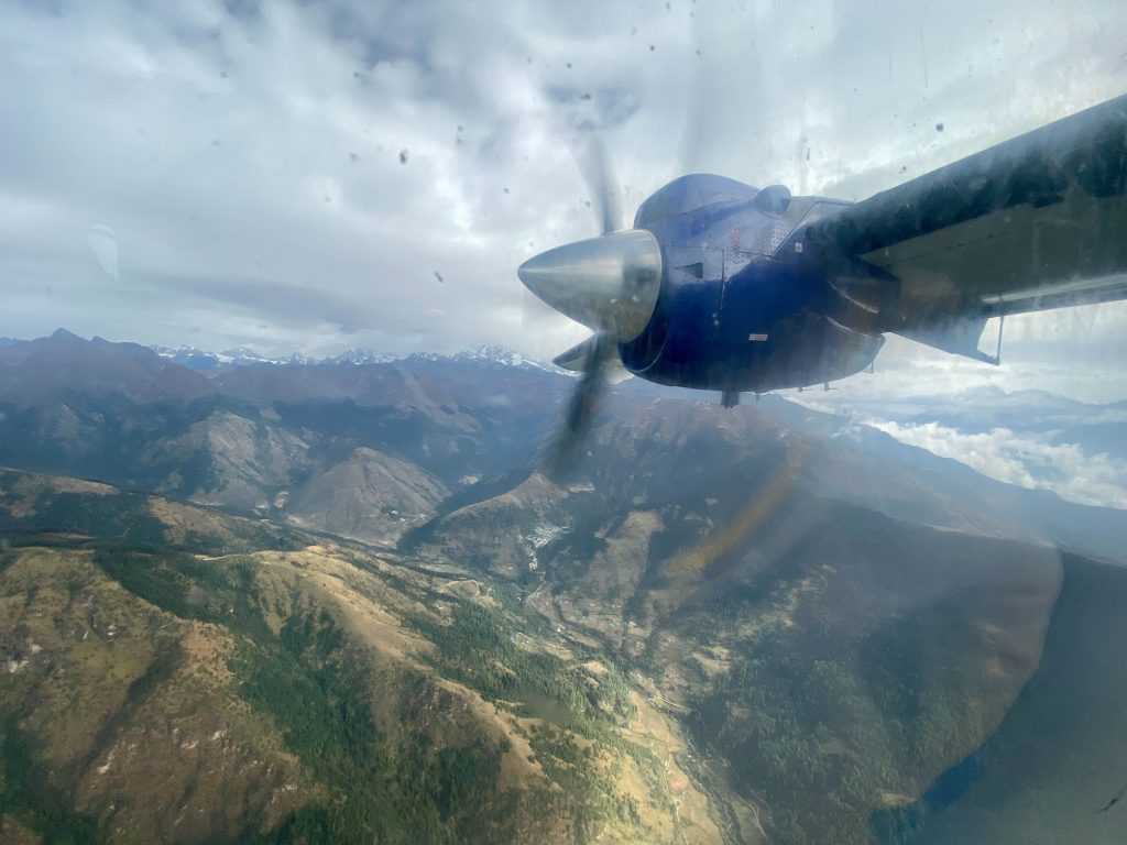 An airplaine flys through the sky with its rudder spinning ... mountains and valleys are below.