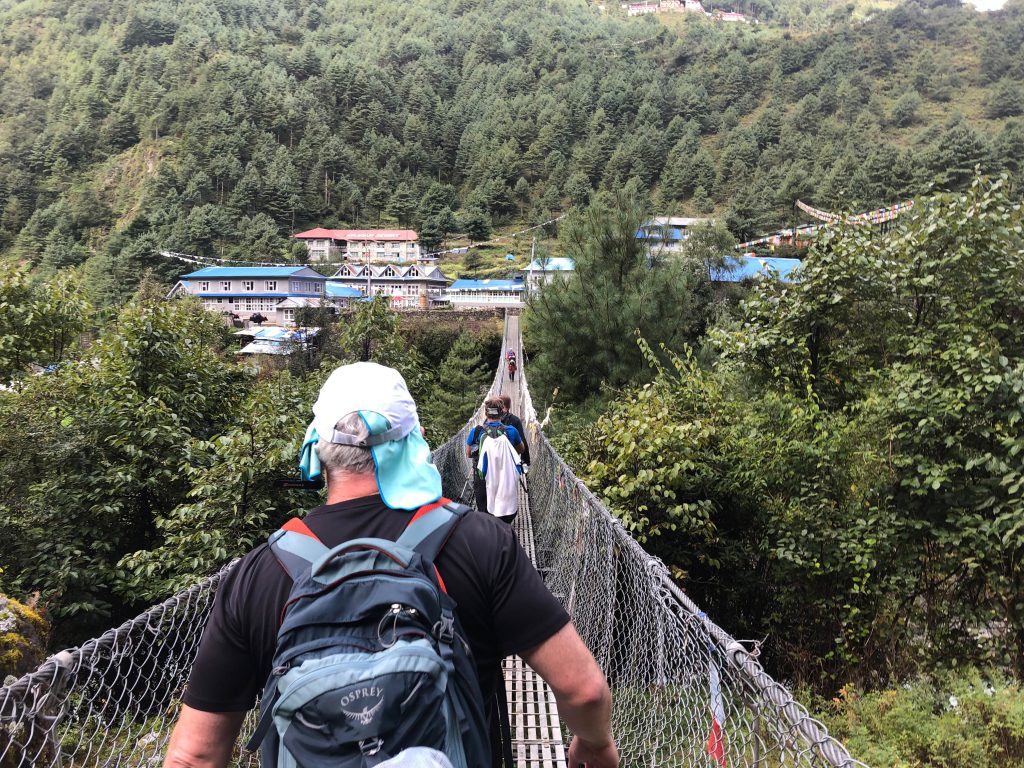 The back of one of the researchers is shown crossing a suspended bridge on the trek.