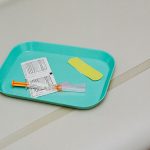 stock photo shows a blue tray with a hypodermic needle on it and a yellow bandaid.
