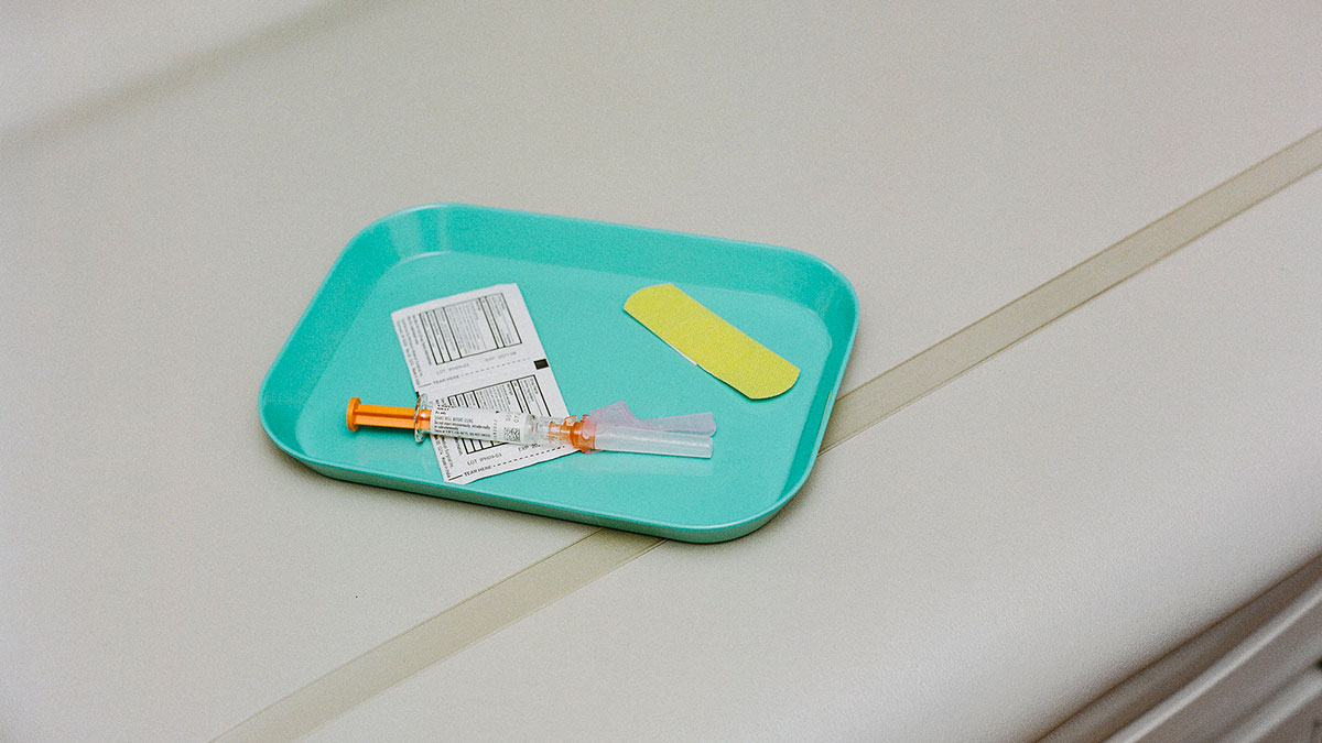 stock photo shows a blue tray with a hypodermic needle on it and a yellow bandaid.