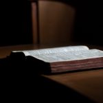 photo shows an open Bible with a bookmark, lying on a table.