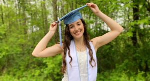 Lauren Revis in graduation cap in a yard. Wearing a white dress.