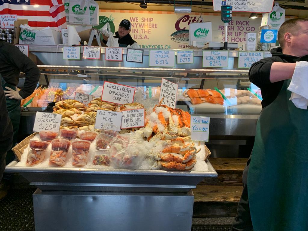 A seafood market shows a case of seafood with customers shopping.