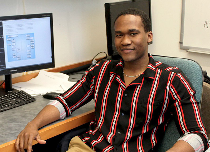 Derrick Carr’s research focuses on how galaxies known as blue nuggets form, generate stars and evolve into a later stage known as red nuggets. He is pictured sitting in front of a computer at his desk.
