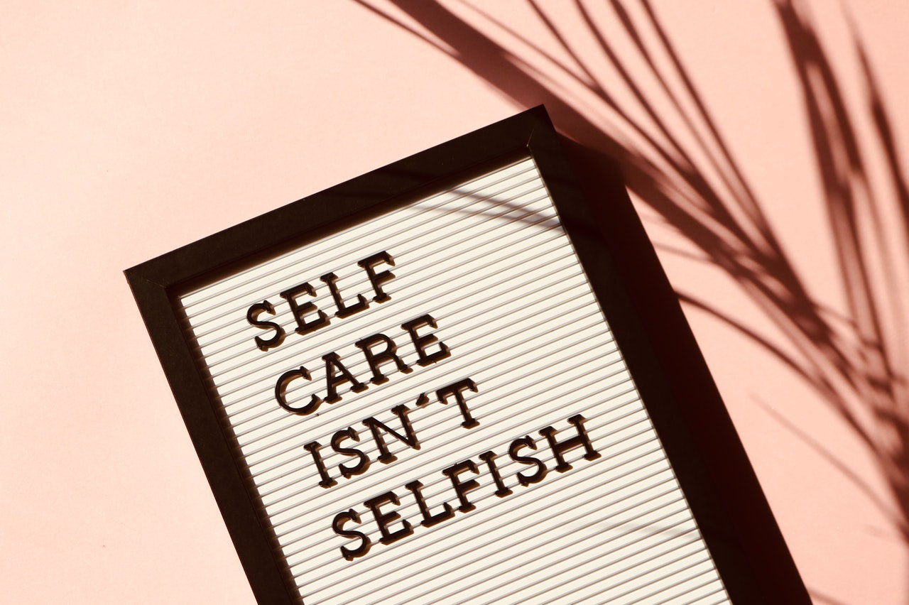 Image on a board says "Self Care Isn't Selfish." Pexels photo by Madison Inouye