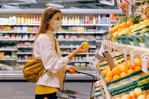 A white masked woman shops for food at a grocery store.