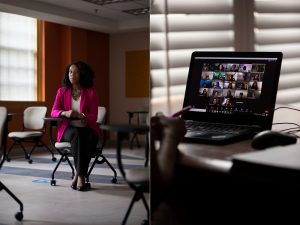 Cassandra R. Davis sits in an empty classroom. A laptop shows a Zoom meeting of a class.