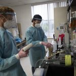 Two graduate students in PPE gear working in a lab