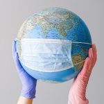 Closeup of two gloved hands holding up a globe with a mask on it.