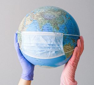 Closeup of two gloved hands holding up a globe with a mask on it.