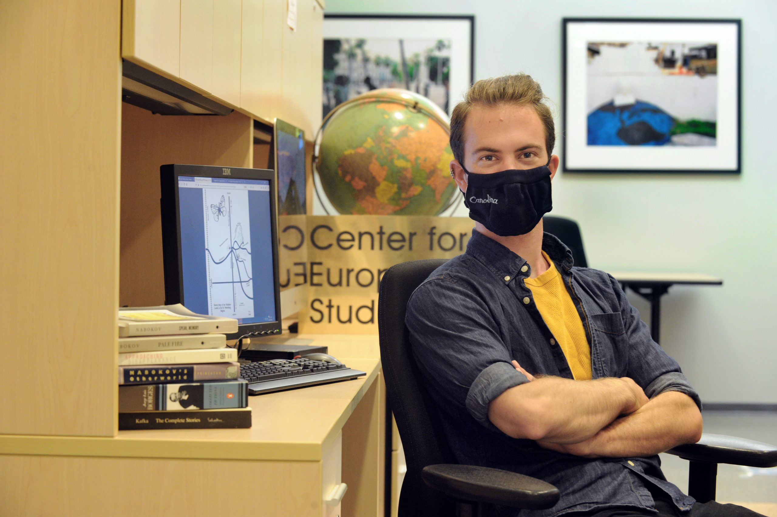 Brett Harris sits in front of a desk with a globe and books. He is wearing a mask.