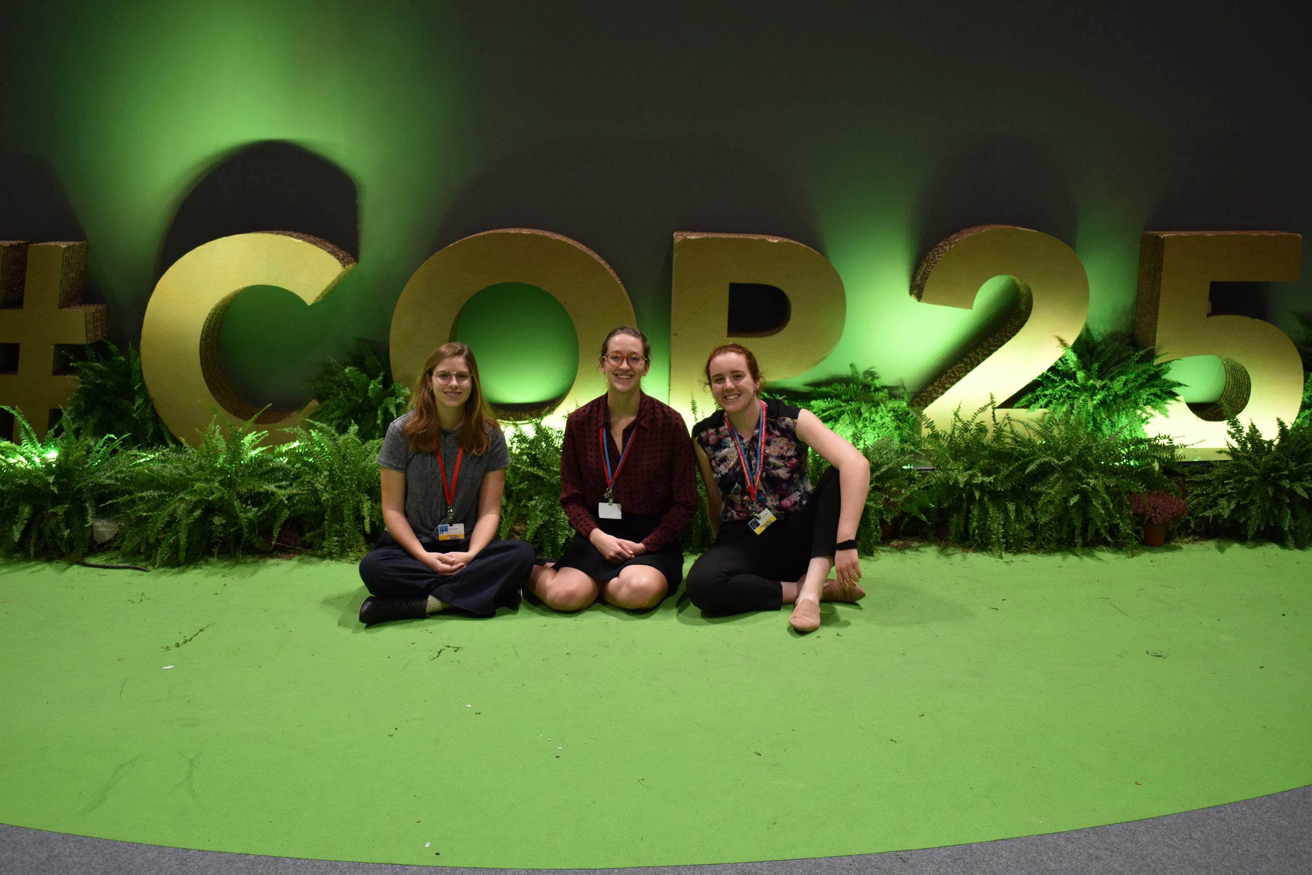 Megan Raisle (right) surrounded by two people in front of a COP 25 sign.