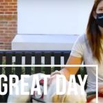 Woman sits on bench with dog. She's wearing a mask. The words It's a Great Day are written on the photo.