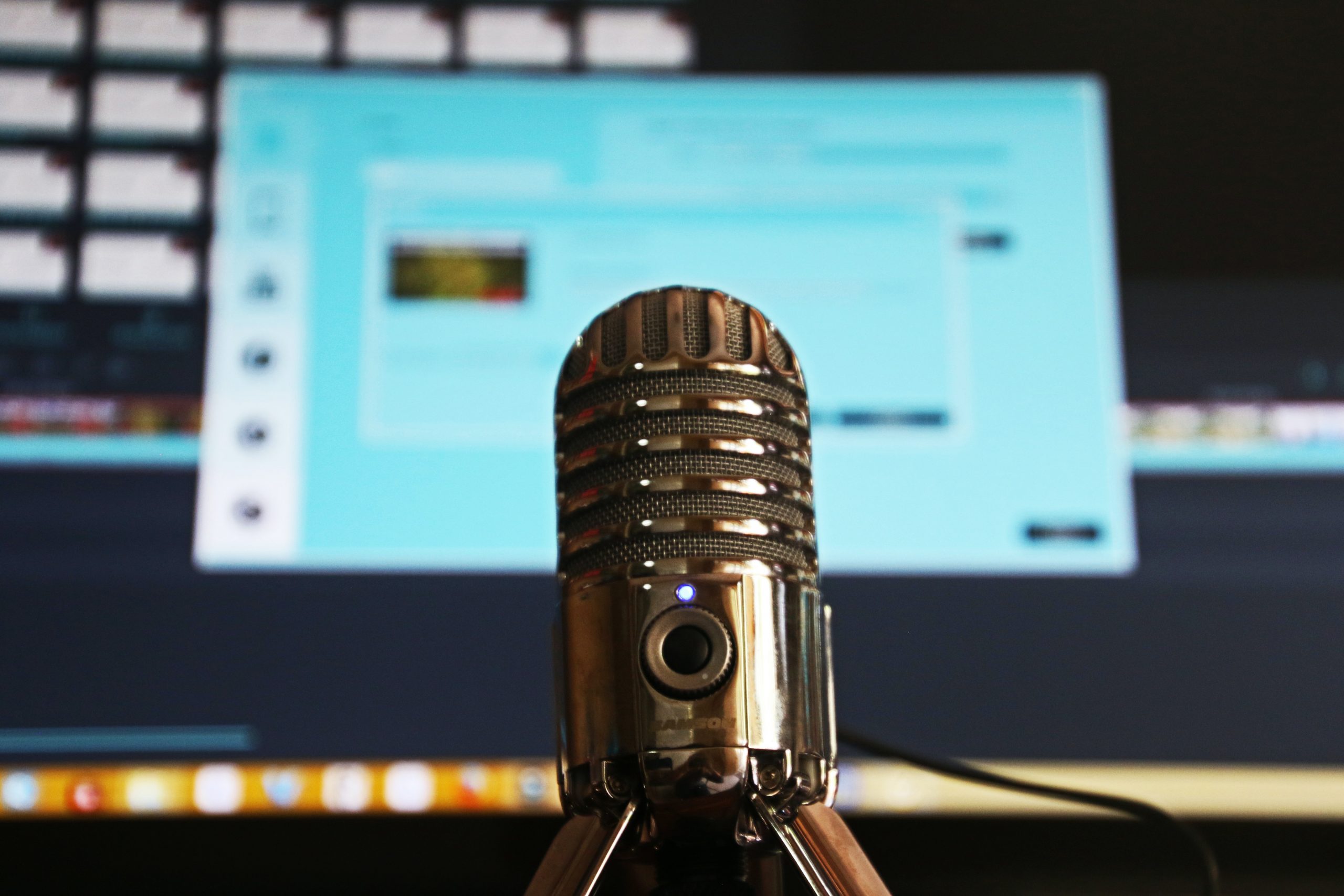 Big podcast-style audio microphone sits in front of a computer screen.