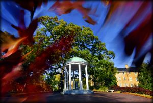 A view through orange-red fall leaves of a blue sky overlooking the Old Well on the Carolina campus. (photo by Donn Young)