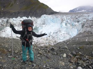 Russler stands with backpack and hiking gear in front of an icy mountain in Alaska.