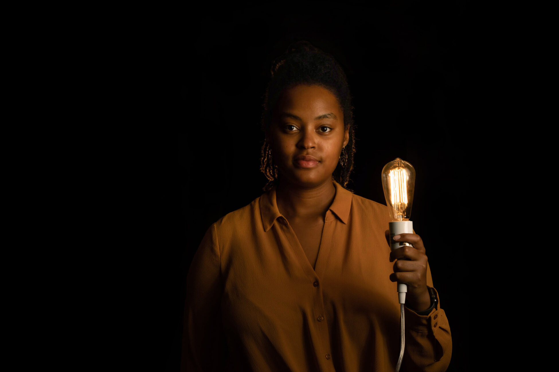 Lenore Hango holds a lighted flashbulb in the darkness around her.