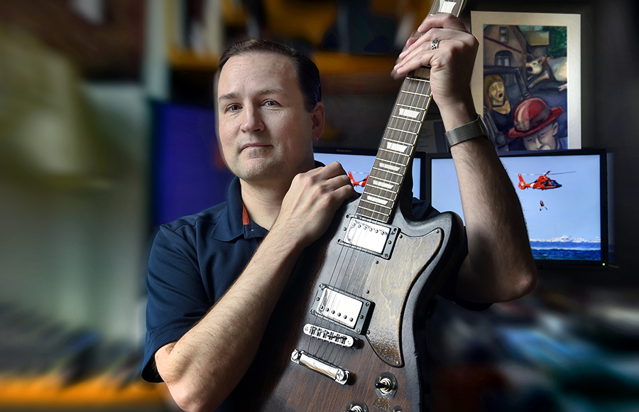 Baskin Cooper holds an electric guitar he made and sits in front of a computer screen in Murray Hall.