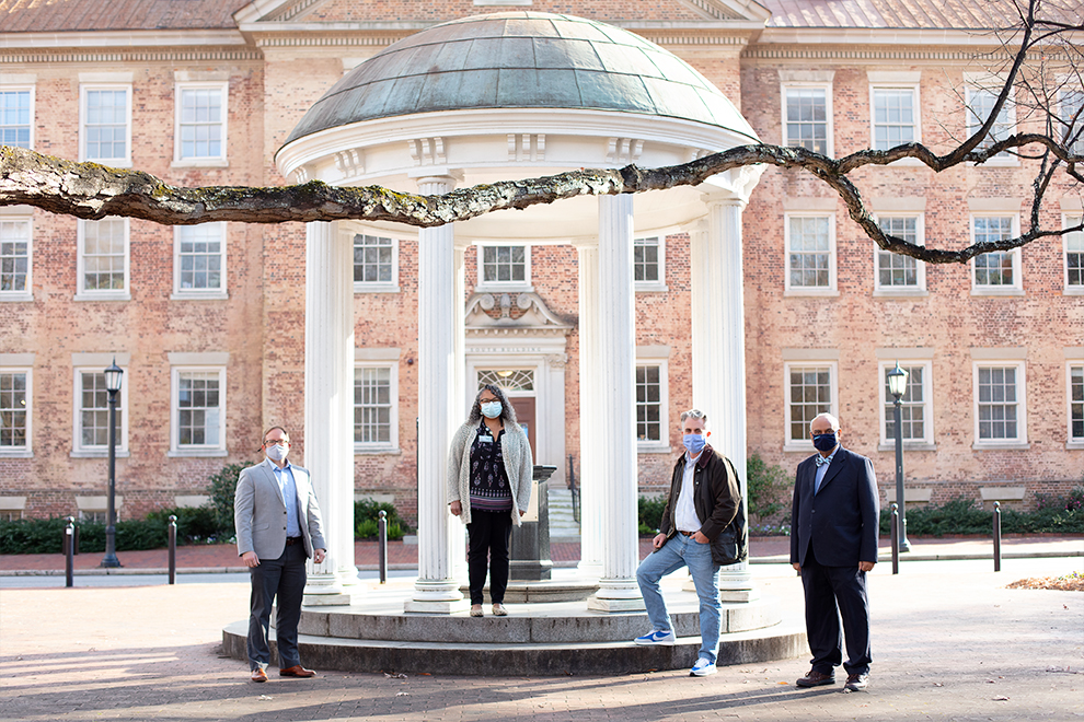 From left to right, masked in front of the Old Well: Jason Cramer, Director of Experiential Professional Development, Suzanne Barbour, Dean of the Graduate School, Jeffrey Warren, Executive Director of the NC Policy Collaboratory, and Deb Aikat, Associate Professor, Hussman School of Journalism and Media. Not pictured: Malinda