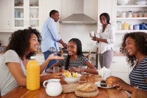 An African American family sits around the kitchen table talking.