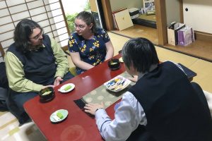 Photo of Smith and his wife look at each other at a table opposite of a Tenrikyo practitioner