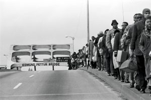 Marchers march over the Edmund Pettus Bridge carrying suitcases and satchels.