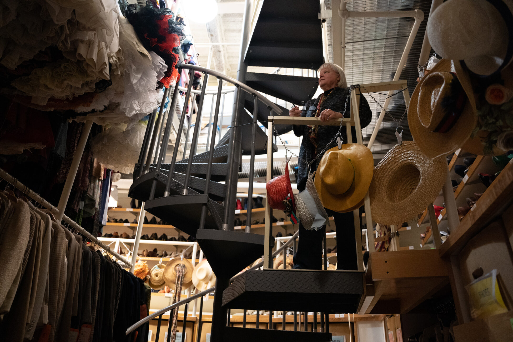 Bobbi Owen stands on a staircase surrounded by costumes.