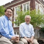 Left, Jianping Lu and right, Otto Zhou sit on a wall in front of Phillps Hall.