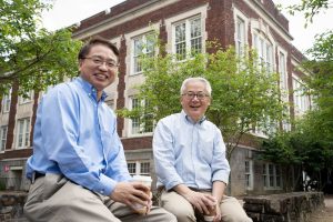 Left, Jianping Lu and right, Otto Zhou sit on a wall in front of Phillps Hall.