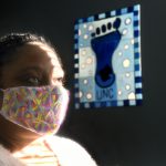 Shayla Evans-Hollingsworth, wearing a mask, looks up as a UNC footprint poster is in the background. Photo by Donn Young.