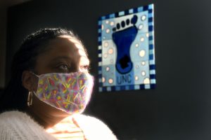 Shayla Evans-Hollingsworth, wearing a mask, looks up as a UNC footprint poster is in the background. Photo by Donn Young.