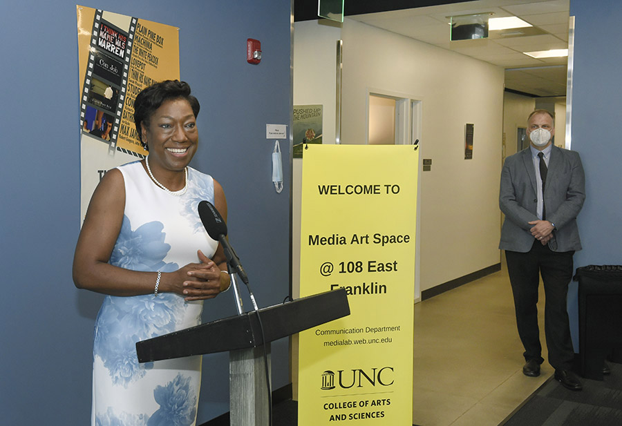 Communication chair Pat Parker stands at the podium with a yellow Media Art Space sign beside her.