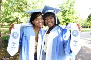 Liz Howard and Aubree Dixon in their graduation caps and gowns, show off their stoles reading Class of 2021.
