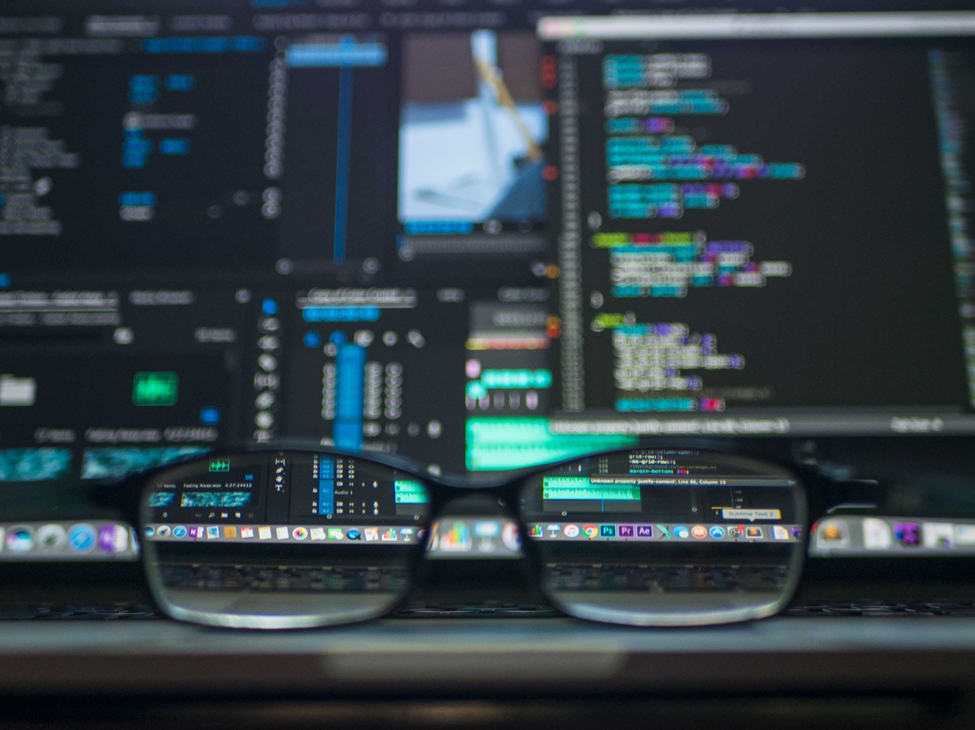 A pair of black glasses sits in front of a computer screen with lots of data on the screen. photo courtesy of pexels.