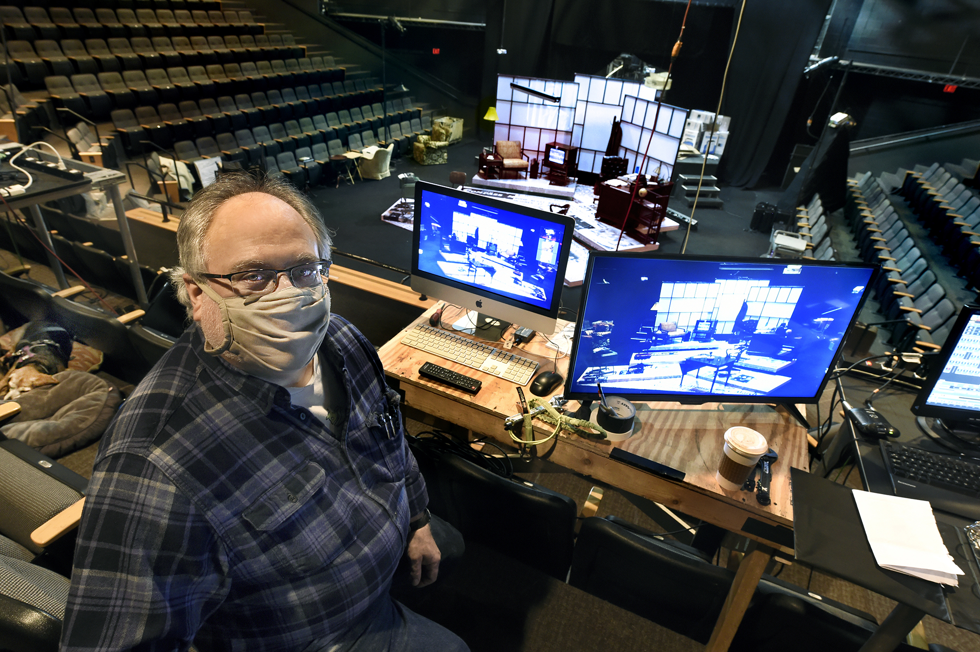 Michael Rolleri, wearing a mask, sits in the production booth of Paul Green Theatre up high in the theater.