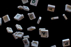 Scrabble pieces are tossed in the air on a black background.