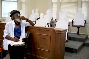 Playwright Thomas Park listens to a rehearsal while sitting in front of cut-outs representing an all-white jury. (photo by Glenn Hinson)