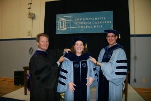 Kevin Guskiewicz, Jason and Joana all smiling at a doctoral hooding ceremony