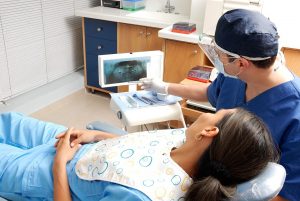 A female dental patient lays in a chair while a dental professional discusses things with her in an exam.