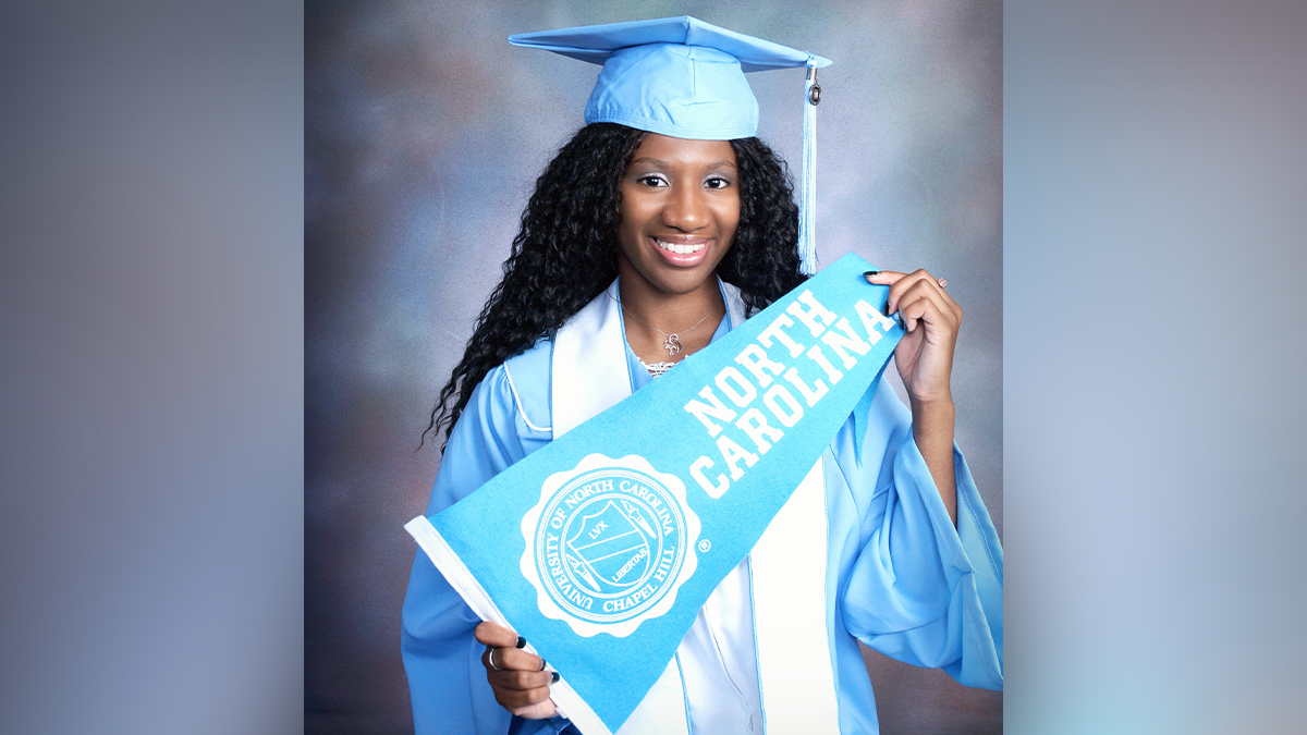 Jocelyn Rives in her cap and gown holding a Carolina banner.