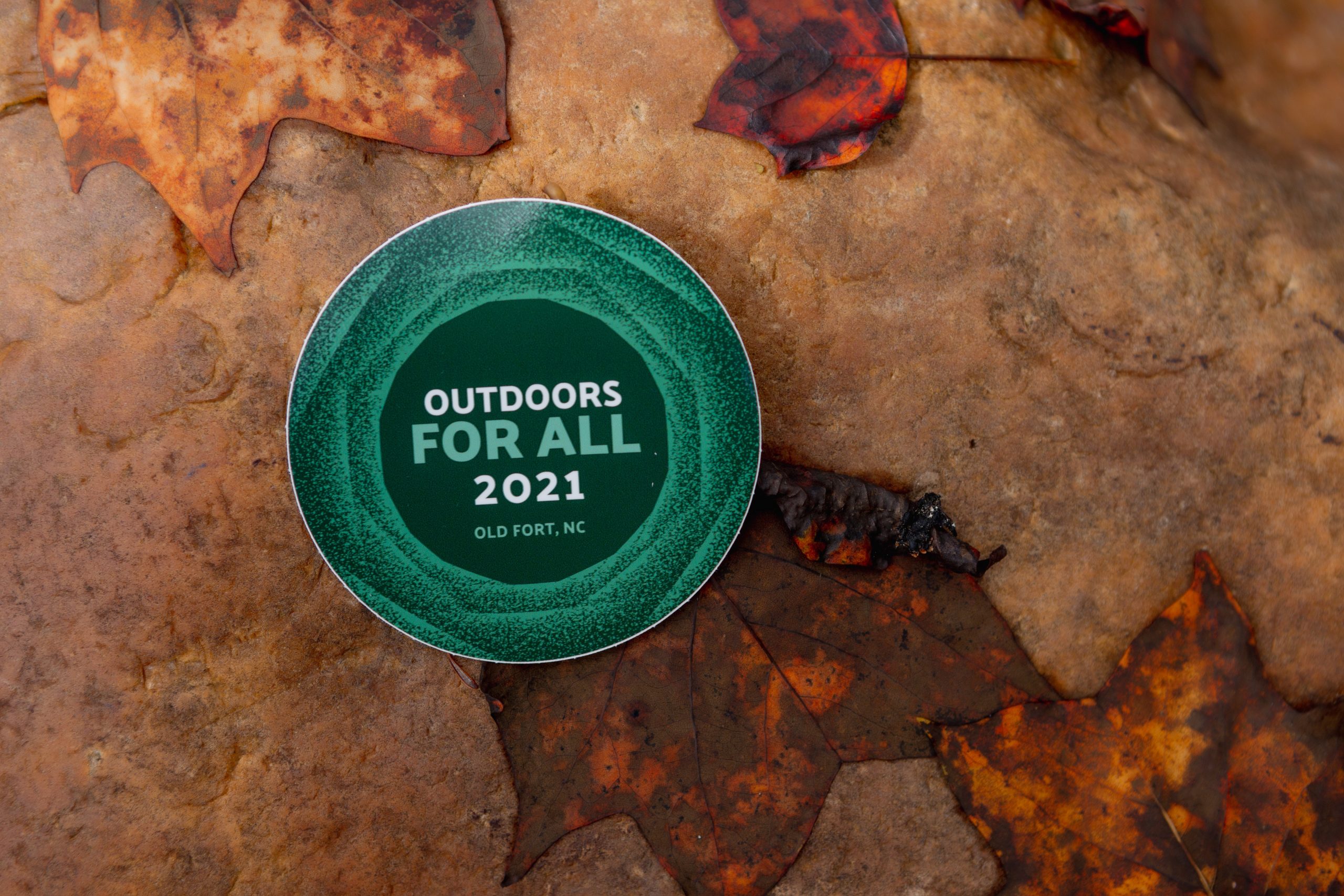 A button says "Outdoors for All 2021" and sits on a bed of scattered leaves.