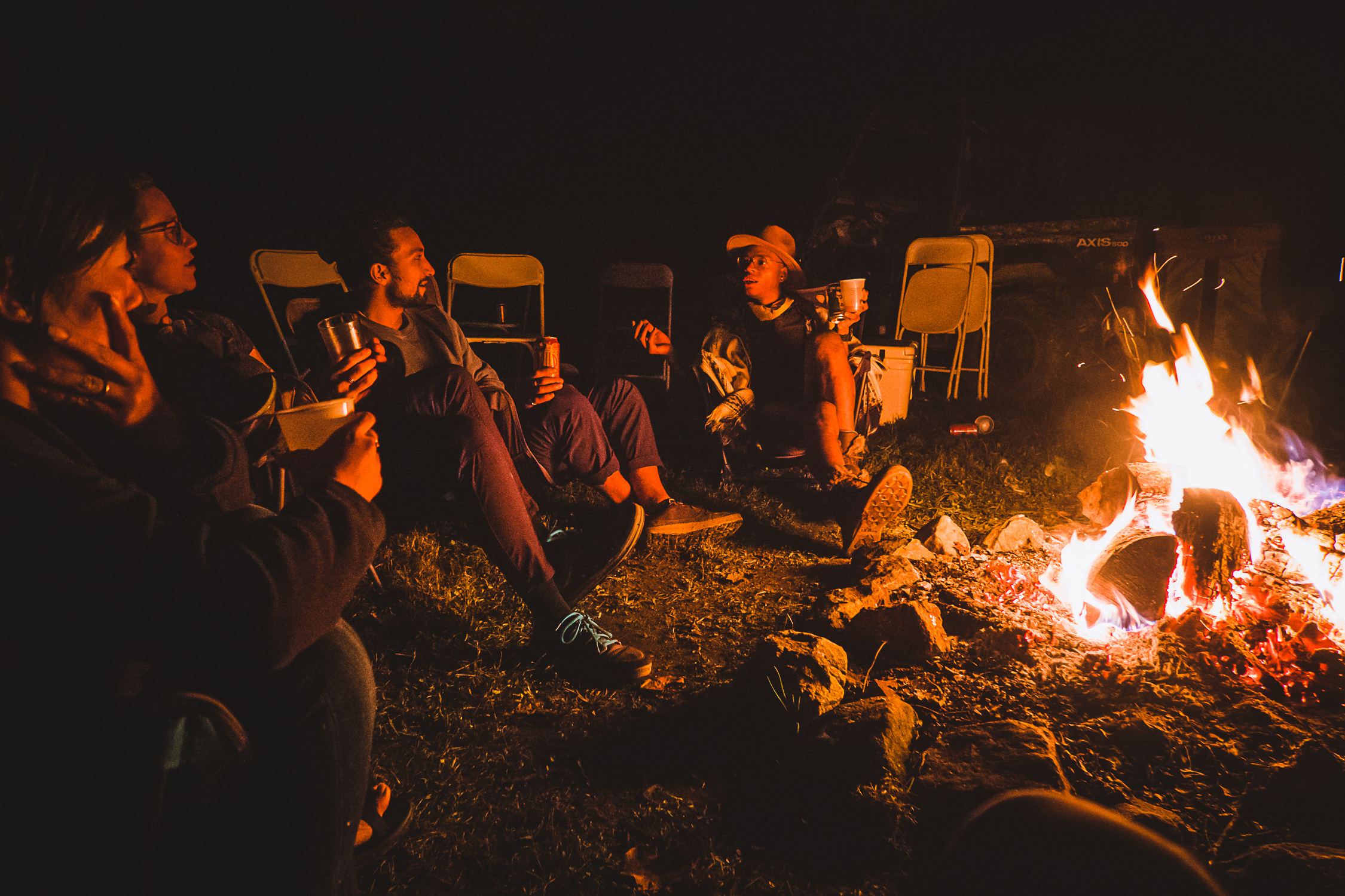 Folks sit around a campfire outside at night.
