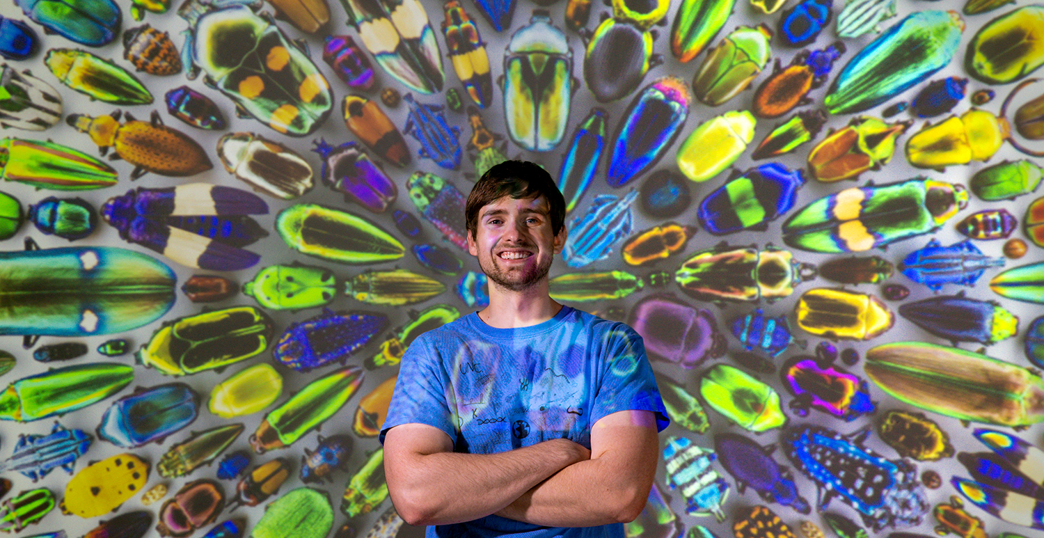 Brian Lerch stands in front of an enlarged image of colorful beetles.