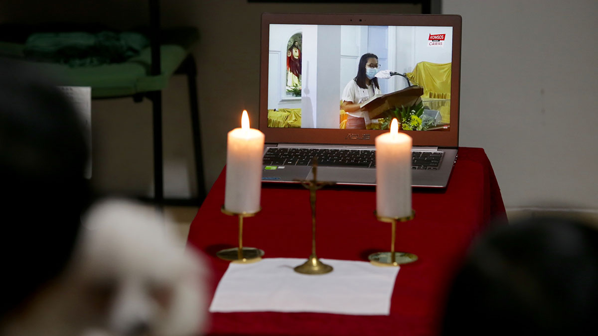 Candles are illuminated on an altar table in front of a computer screen where a worship service is going on.