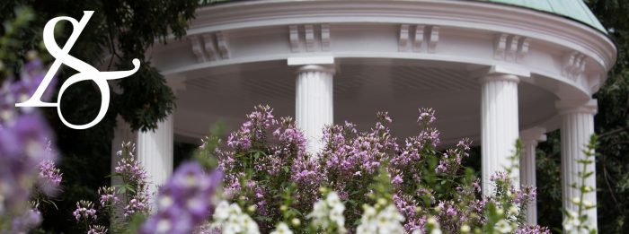 Social media cover of white and purple flowers in front of the Old Well with the College of Arts & Sciences ampersand