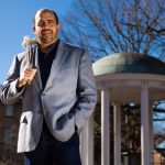 Juan Alamo standing at the Old Well on UNC-Chapel Hill's campus holding a percussion instrument