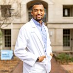 A photo of Brandon Feaster in a white lab coat on UNC-Chapel Hill's campus