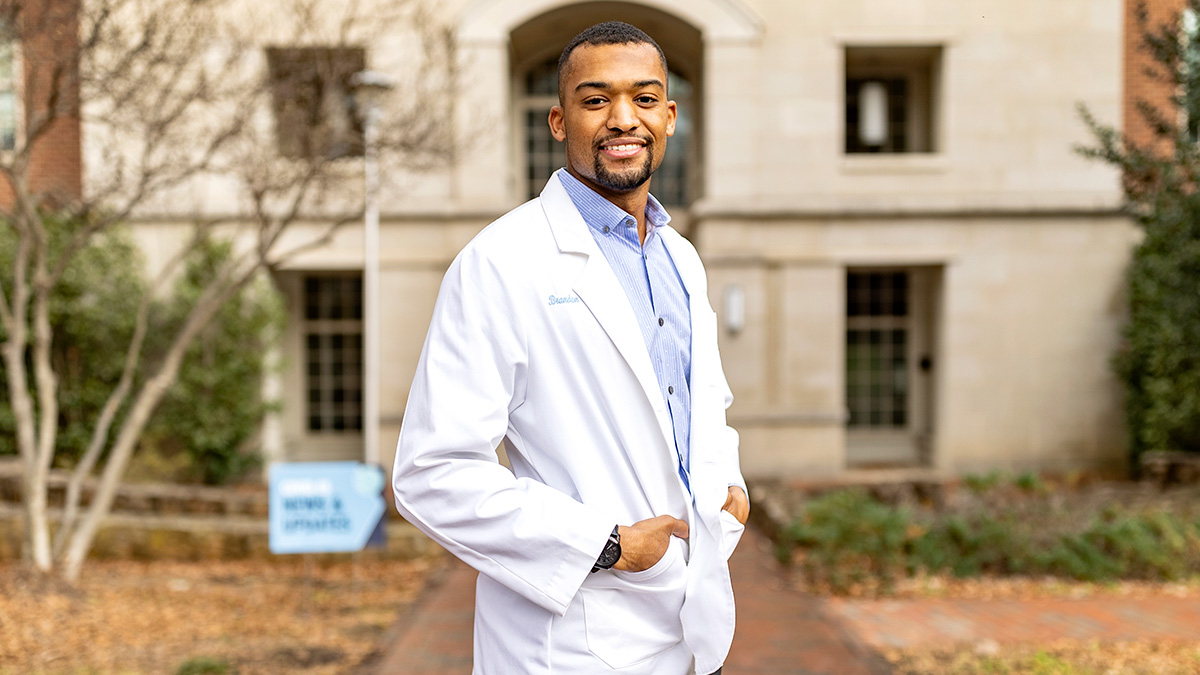 A photo of Brandon Feaster in a white lab coat on UNC-Chapel Hill's campus