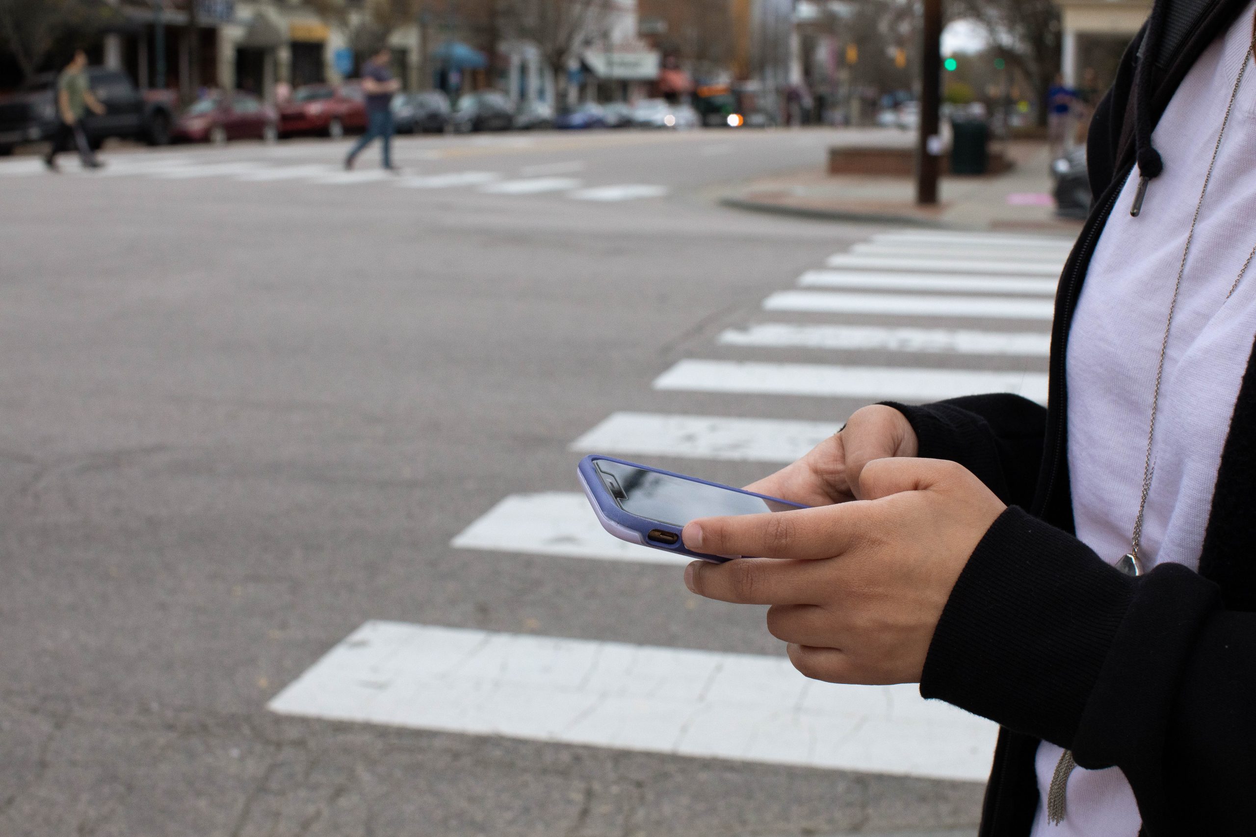A photo illustration depicting the impacts of social media on mental health in teenagers (Photo by Jeyhoun Allebaugh/UNC-Chapel Hill). A teen holds a cell phone while walking across the street.