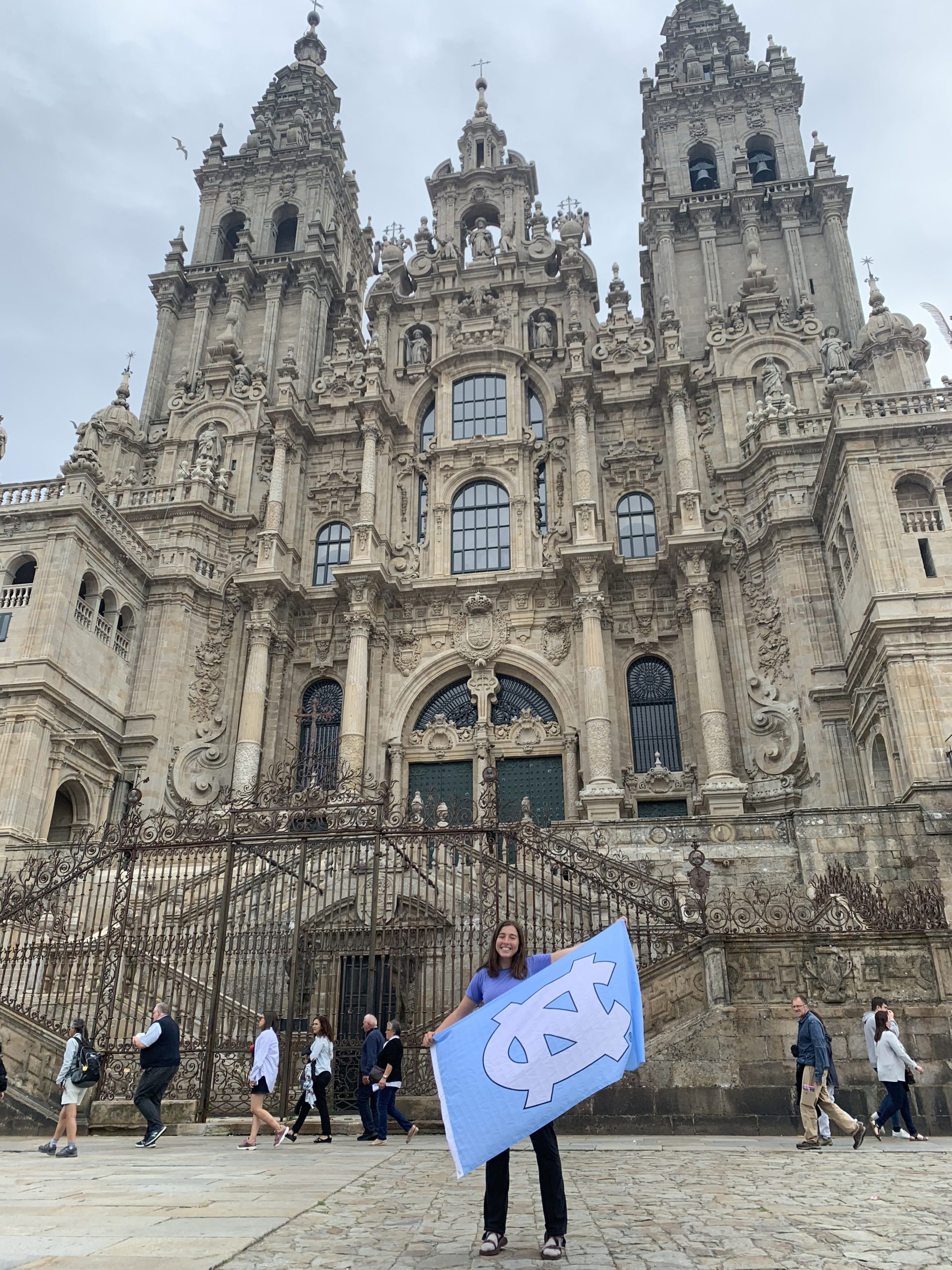 Alaina stands in front of a church in Spain holding a UNC flag.